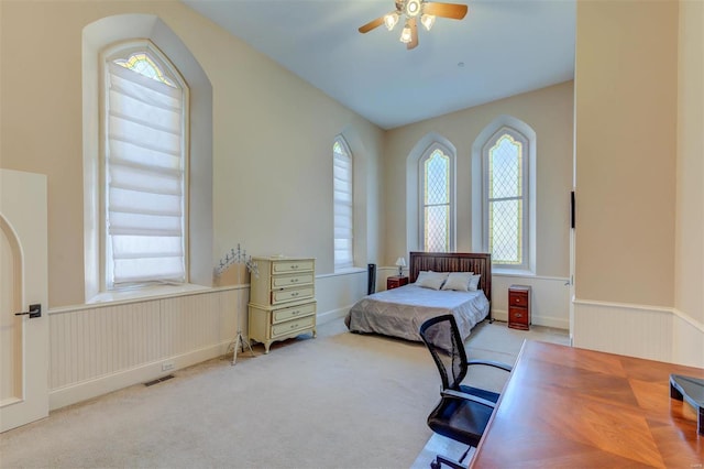 bedroom with visible vents, ceiling fan, a wainscoted wall, carpet floors, and arched walkways