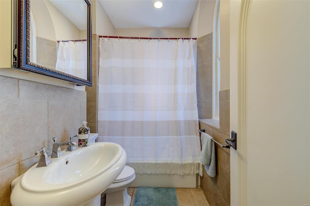 bathroom featuring tile patterned flooring, toilet, shower / bath combo, tile walls, and a sink