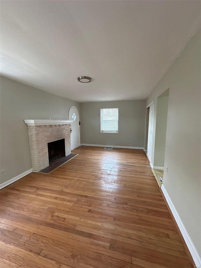 unfurnished living room featuring visible vents, a brick fireplace, baseboards, and wood finished floors