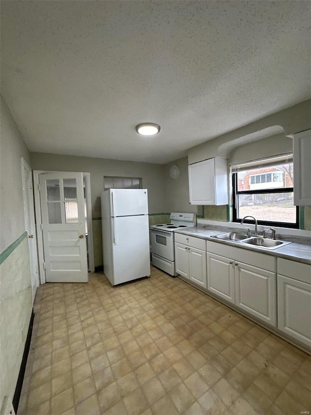 kitchen featuring white appliances, light floors, a sink, a textured ceiling, and white cabinetry