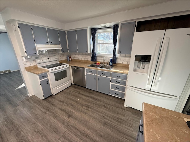 kitchen featuring a sink, gray cabinetry, under cabinet range hood, white appliances, and dark wood-style flooring