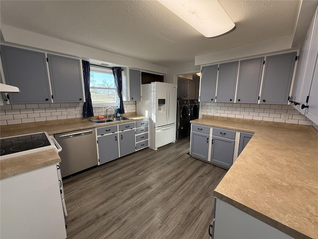 kitchen with dark wood-type flooring, a sink, white refrigerator with ice dispenser, separate washer and dryer, and dishwasher