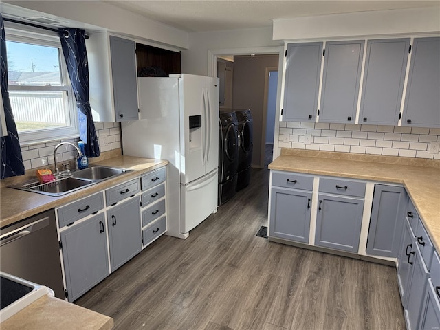 kitchen featuring gray cabinetry, a sink, stainless steel dishwasher, dark wood-style flooring, and washing machine and clothes dryer