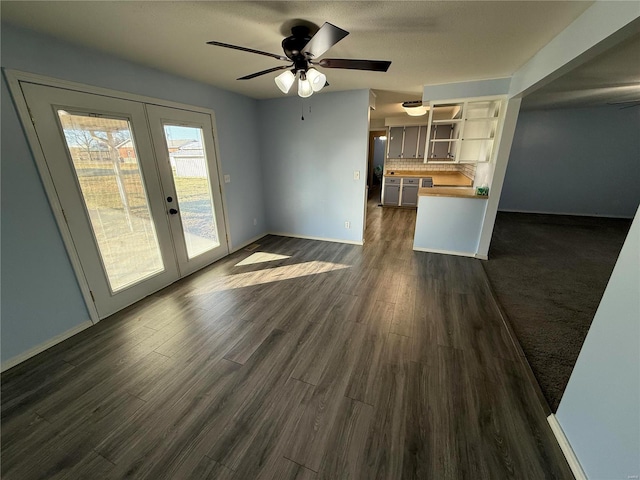 unfurnished living room featuring french doors, baseboards, dark wood-type flooring, and ceiling fan