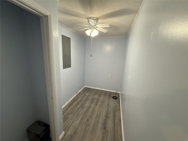 empty room with a ceiling fan, electric panel, a textured ceiling, baseboards, and dark wood-style flooring