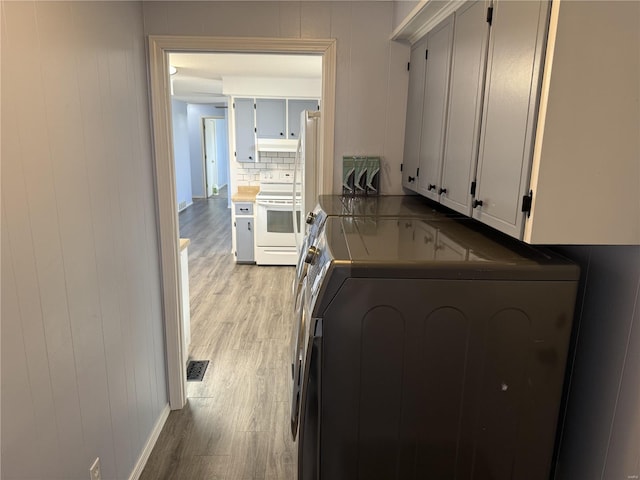 kitchen with visible vents, washer and dryer, white electric stove, light wood-style floors, and decorative backsplash