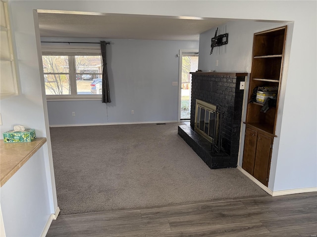 living room with a brick fireplace, plenty of natural light, baseboards, and dark carpet