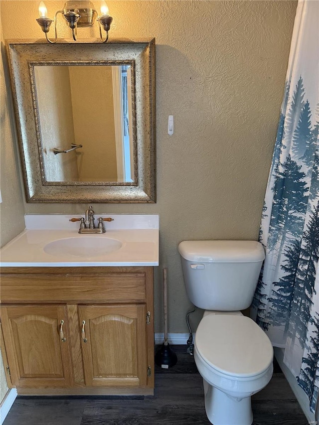 bathroom featuring toilet, wood finished floors, baseboards, vanity, and a textured wall