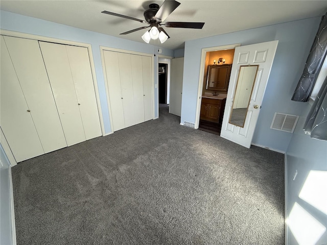 unfurnished bedroom with visible vents, dark carpet, a ceiling fan, and multiple closets