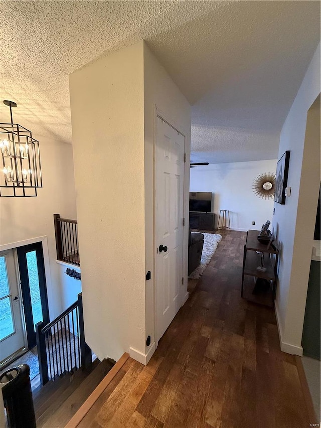 hallway with baseboards, dark wood finished floors, a chandelier, an upstairs landing, and a textured ceiling