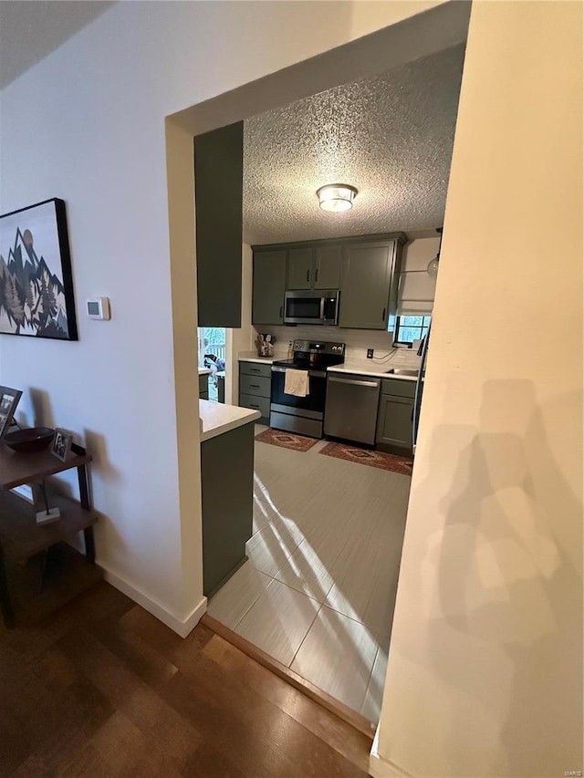 kitchen featuring baseboards, light countertops, appliances with stainless steel finishes, wood finished floors, and a textured ceiling