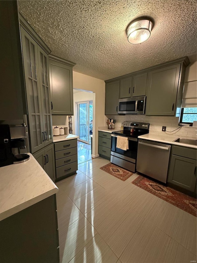 kitchen with gray cabinetry, a sink, backsplash, stainless steel appliances, and light countertops