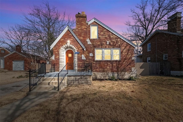 tudor-style house featuring brick siding, a chimney, a yard, and fence