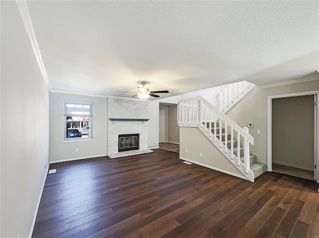 unfurnished living room with a brick fireplace, crown molding, stairway, dark wood-style floors, and a textured ceiling