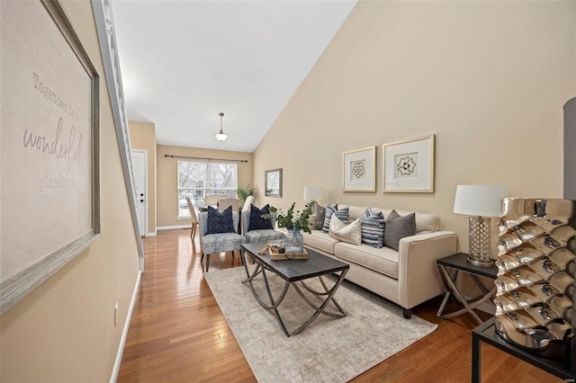 living area featuring arched walkways, wood finished floors, baseboards, and high vaulted ceiling