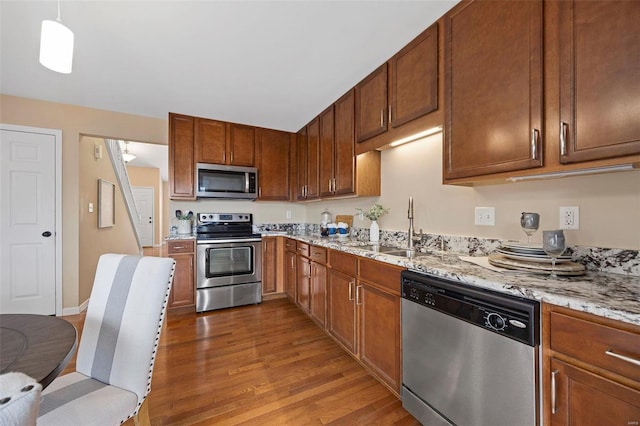 kitchen featuring light stone counters, appliances with stainless steel finishes, wood finished floors, and a sink