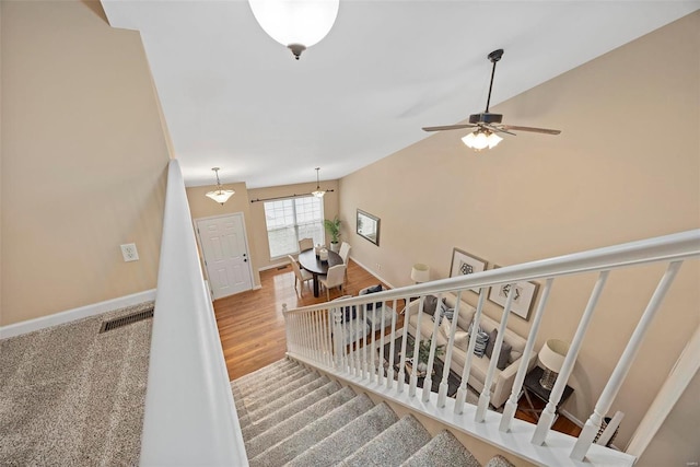 stairway with wood finished floors, visible vents, baseboards, ceiling fan, and vaulted ceiling