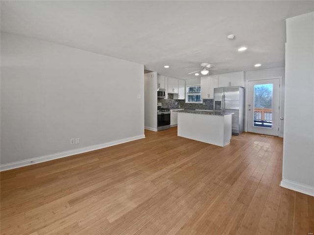 kitchen featuring baseboards, light wood finished floors, stainless steel appliances, white cabinets, and backsplash