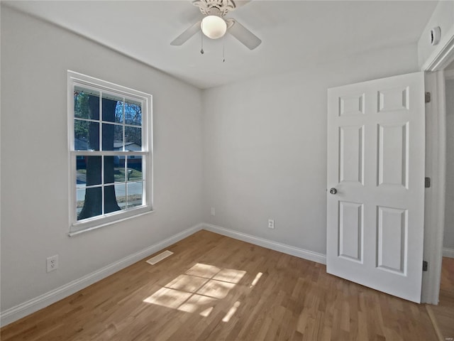 unfurnished room with ceiling fan, wood finished floors, visible vents, and baseboards