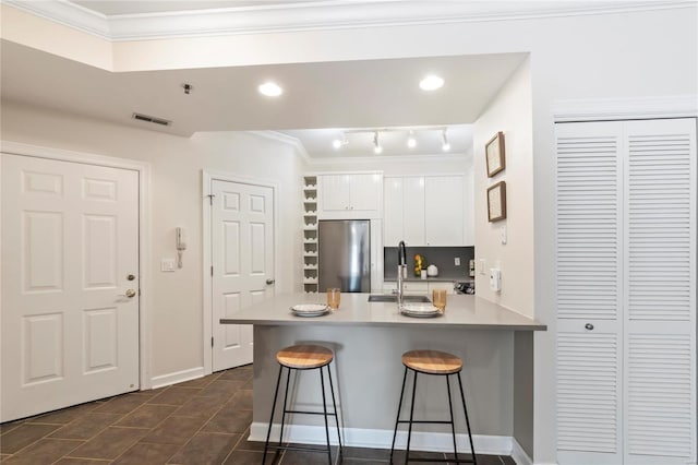 kitchen featuring visible vents, a kitchen bar, white cabinetry, freestanding refrigerator, and a peninsula