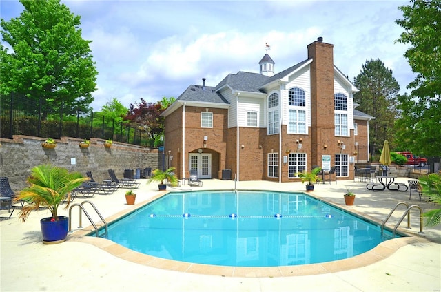 outdoor pool with a patio area, fence, and french doors