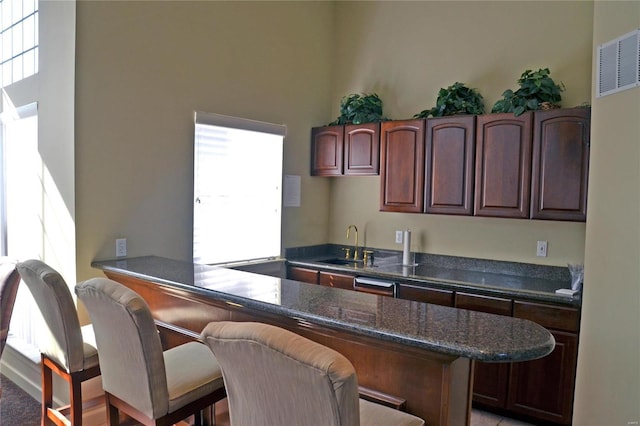 kitchen with a kitchen bar, visible vents, a sink, dark stone countertops, and a peninsula