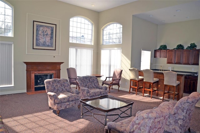 living room featuring a fireplace with flush hearth, baseboards, a towering ceiling, and carpet floors