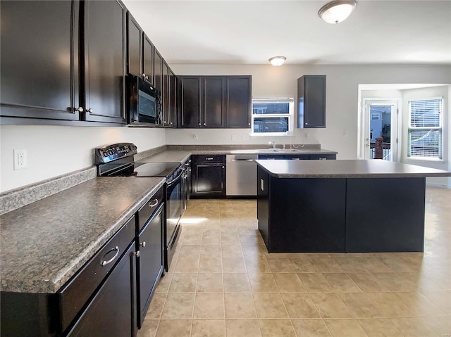 kitchen with black appliances, a center island, dark countertops, and a sink