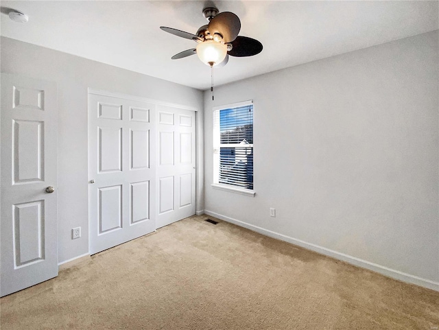 unfurnished bedroom with a ceiling fan, visible vents, baseboards, a closet, and light colored carpet