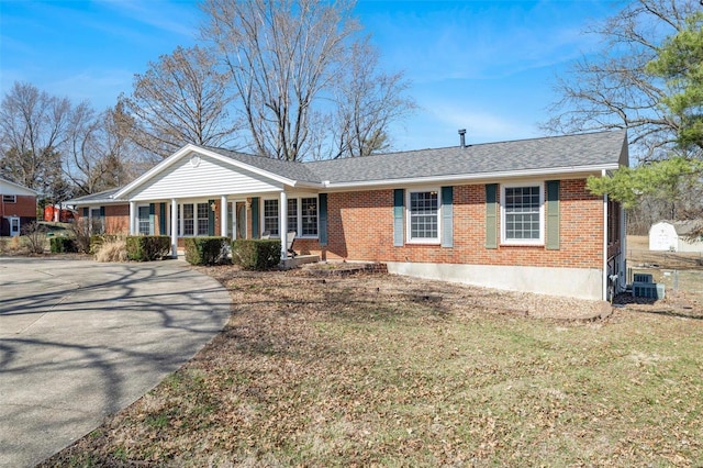 view of front of house with cooling unit, brick siding, a porch, and a front yard