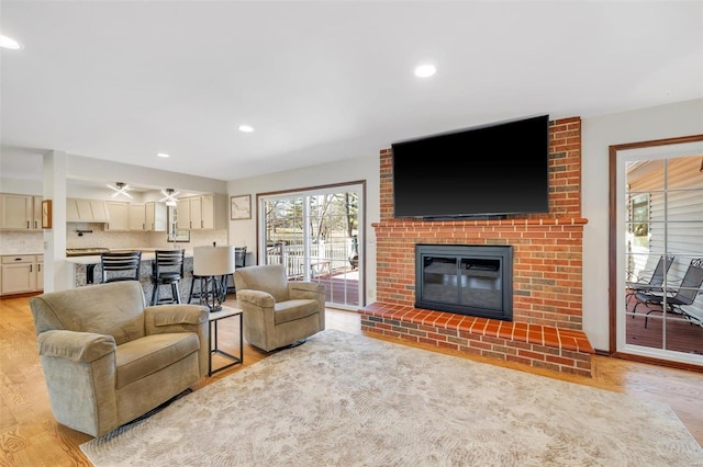 living room featuring recessed lighting, light wood-style flooring, and a brick fireplace