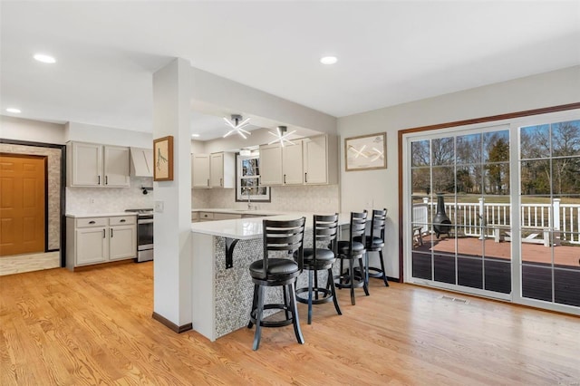 kitchen featuring stainless steel range with electric stovetop, light wood-style flooring, a kitchen breakfast bar, backsplash, and light countertops