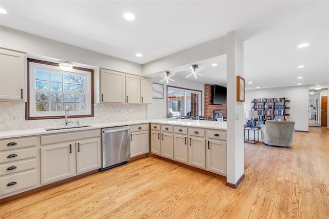 kitchen featuring a sink, light countertops, light wood-style floors, dishwasher, and backsplash