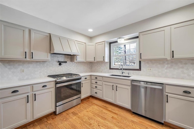 kitchen with light countertops, light wood-type flooring, appliances with stainless steel finishes, custom exhaust hood, and a sink