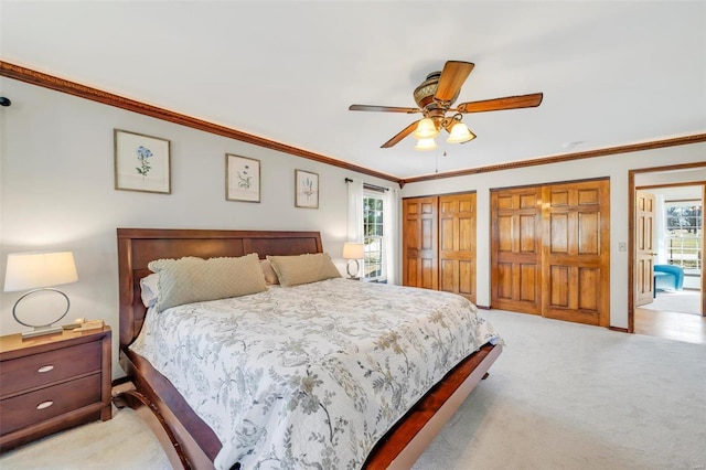 bedroom featuring light colored carpet, a ceiling fan, crown molding, and multiple closets