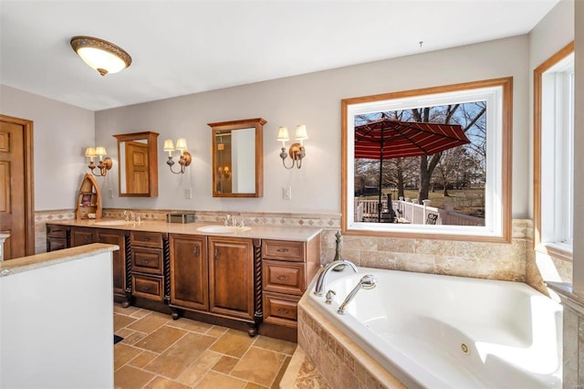 bathroom featuring a sink, stone finish flooring, a tub with jets, and double vanity