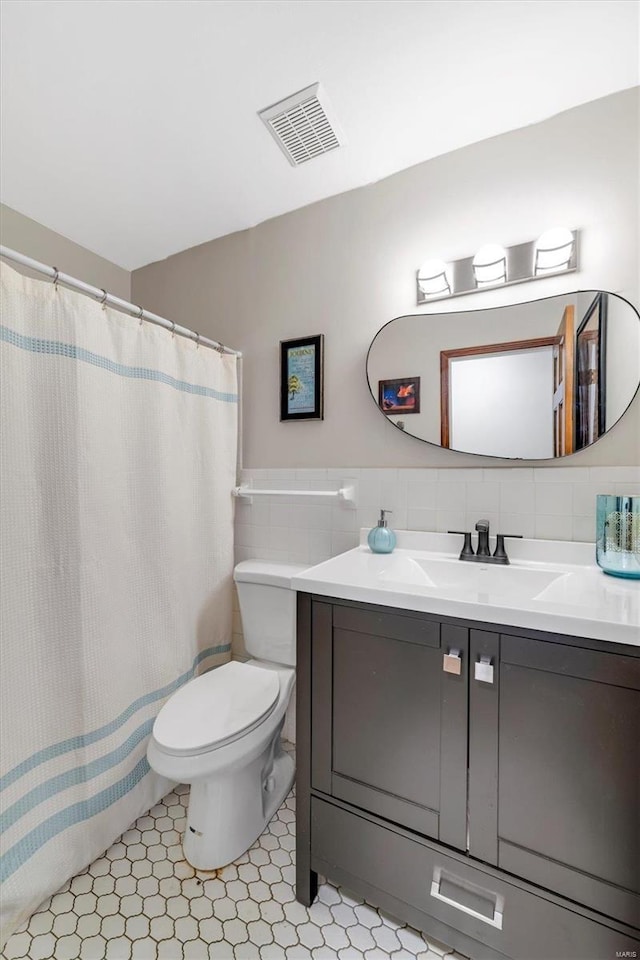 full bath with visible vents, toilet, vanity, and tile walls