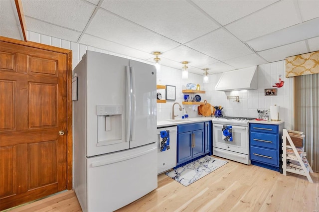 kitchen featuring white appliances, custom exhaust hood, blue cabinetry, light wood-style flooring, and a sink