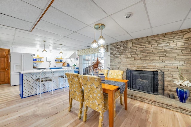 dining area with a drop ceiling, a fireplace, and light wood finished floors