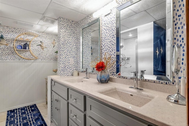 full bath featuring double vanity, tiled shower, visible vents, and a sink