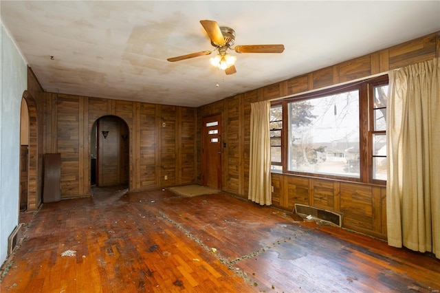 empty room with arched walkways, a ceiling fan, and wood finished floors