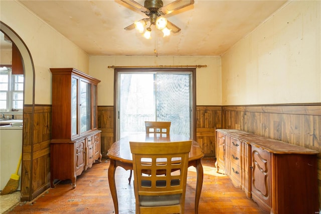 dining space with a wealth of natural light, a wainscoted wall, arched walkways, and light wood-style floors