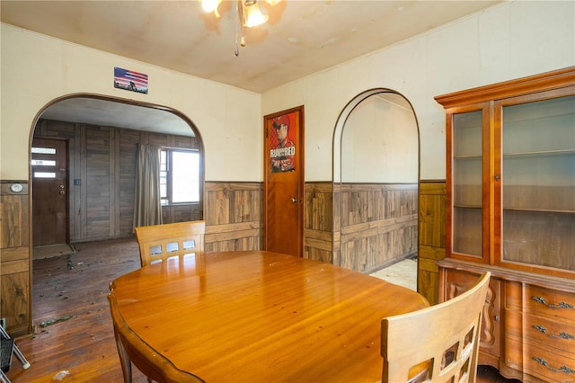 dining area featuring arched walkways, a wainscoted wall, and hardwood / wood-style flooring