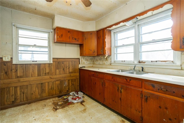 kitchen with wood walls, light floors, light countertops, a ceiling fan, and a sink