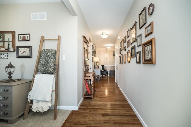 hall featuring visible vents, baseboards, and wood finished floors