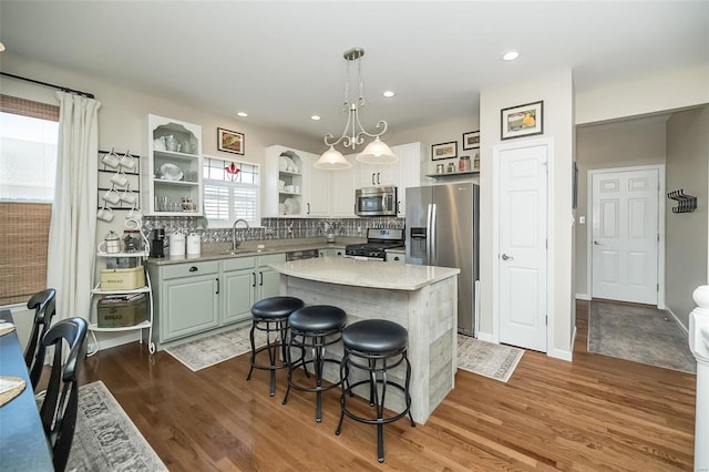 kitchen with wood finished floors, a kitchen island, open shelves, appliances with stainless steel finishes, and a kitchen bar