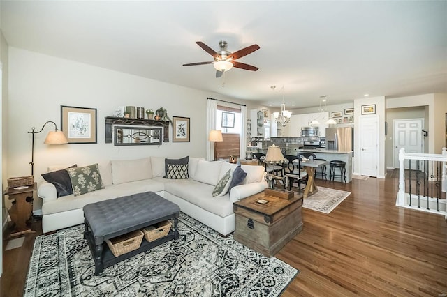 living area featuring dark wood finished floors, ceiling fan with notable chandelier, and baseboards