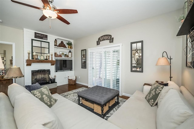 living room with ceiling fan, a fireplace, dark wood-type flooring, and baseboards