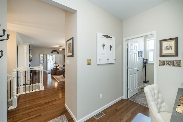 hallway with an upstairs landing, visible vents, dark wood finished floors, and baseboards