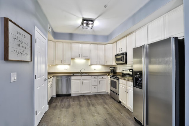 kitchen featuring dark countertops, a sink, backsplash, stainless steel appliances, and dark wood-style flooring